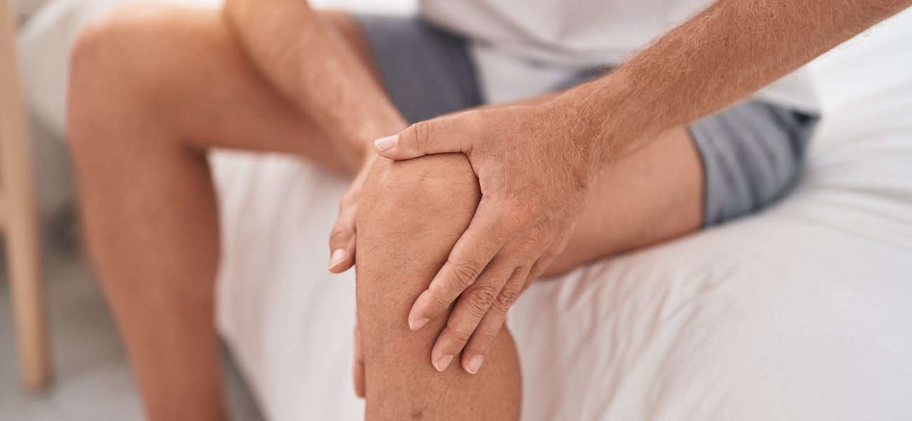 young-blond-man-suffering-knee-injury-sitting-bed-bedroom